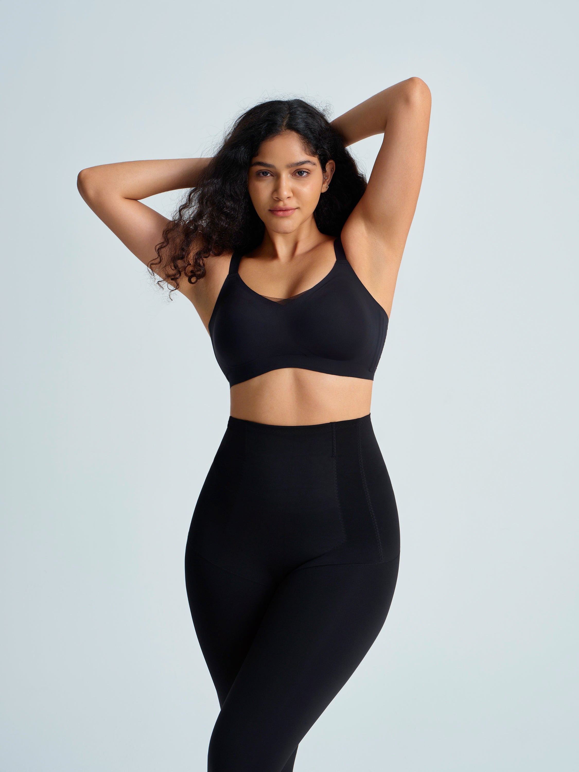 Woman wearing a black sports bra and leggings on a light gray background
